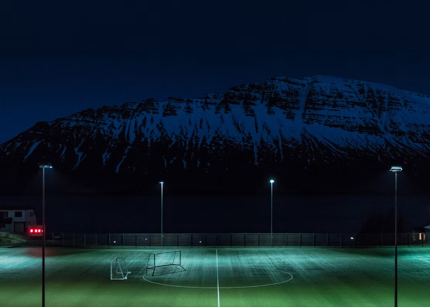 Terrain de football éclairé la nuit devant une montagne enneigée